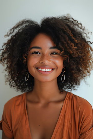 A young woman with naturally curly hair smiles warmly, expressing happiness and confidence against a plain backgroundの素材