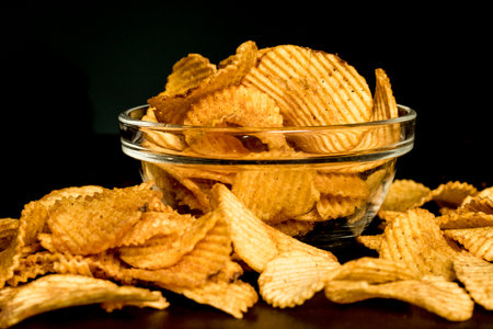 Crispy potato chips in a glass bowl on a black background