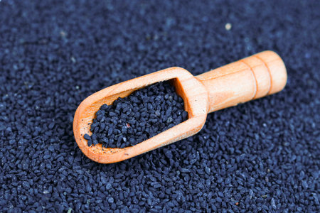 Black Cumin seeds in wooden scoop on black background close up.の写真素材