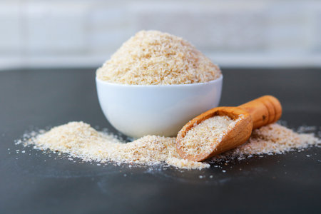 Psyllium Husk (Isabgol) in a bowl with a wooden scoop on a black background