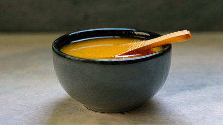Honey in a bowl with wooden spoon on a gray background.