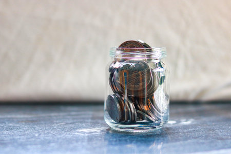 Coins in a glass jar on a gray background. Saving money concept.の写真素材