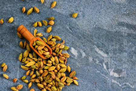 Cardamom spice in a wooden scoop on a stone background.