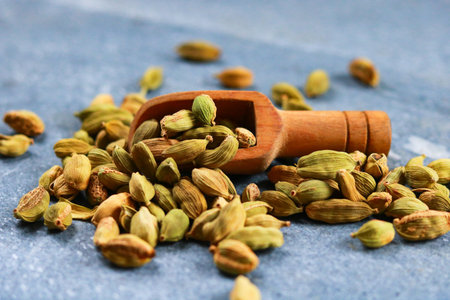 Heap of green cardamom seeds with wooden scoop on blue backgroundの写真素材