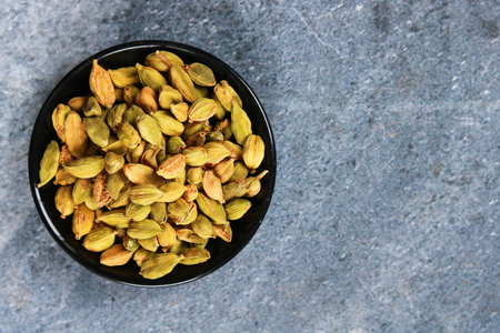 Dried cardamom seeds in a bowl on a stone background, top view