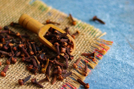 Cloves in wooden scoop on sackcloth and blue wooden background.の写真素材