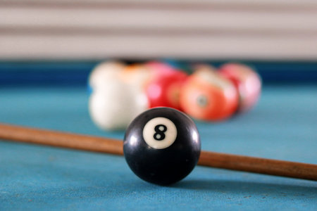 Close-up of black number 8 pool ball on blue billiard table with cue stick