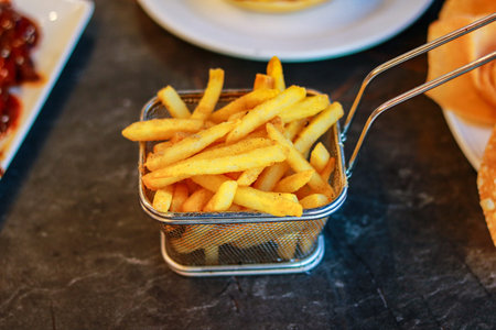 Deep Fried Crispy Potato Fries in Wire Basket Served on a Slate Tableの写真素材