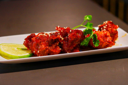 Spicy Korean Fried Chicken Wings with Sesame Seeds and Lime Garnish on White Plateの写真素材