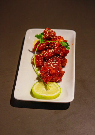 Spicy Korean Fried Chicken Wings with Sesame Seeds and Lime Garnish on White Plateの写真素材