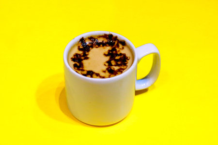 Hot Coffee Latte with Art Foam in White Mug on Vibrant Yellow Backgroundの写真素材