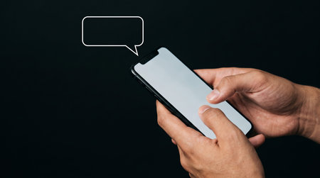 Close up of hand holding smart phone with speech bubble on black background