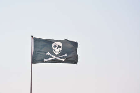Pirate flag with with skull and bones on a light blue sky background.の写真素材
