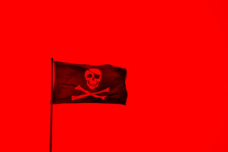 A red coloured pirate flag with with skull and bonesの写真素材
