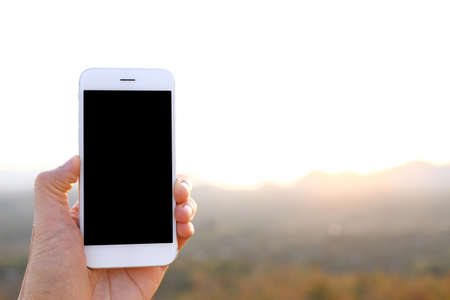 Hand holding mockup smartphone with sunlight and mountain backgroundの写真素材