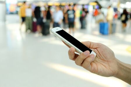 Hand holding smartphone with airport passenger background