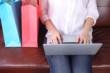 Woman sit on sofa with shooping bag beside and using laptopの写真素材