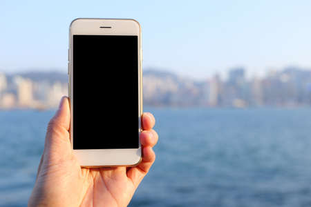 Hand holding smartphone with bay and skyline backgroundの写真素材