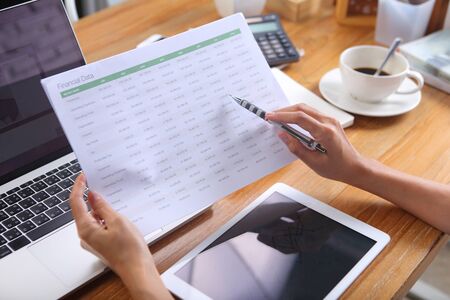 Business woman using pencil point to number on financial data sheet with laptop smartphone and...