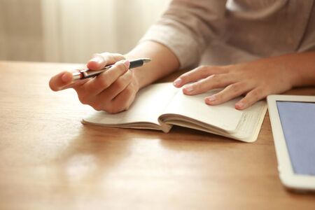 Cluse up business woman writing on paper with tablet mockup on wooden deskの写真素材