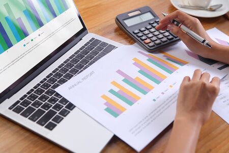 Business woman using calculator calculate annual report with laptop and office stationery on wooden...