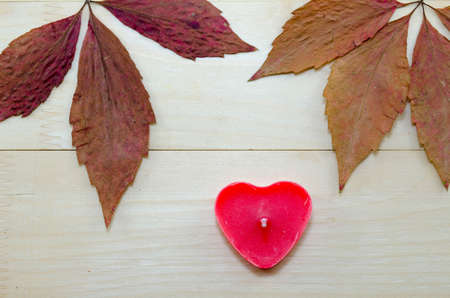 Dry and colorful autumn leaves and a red heart shaped candle on a wooden tableの写真素材