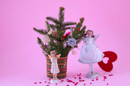 Two angel figurines on pink background, decorated with stars and a fir treeの写真素材