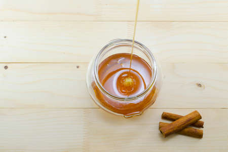 Honey dripping into a glass jar with sticks of cinnamon on a wooden tableの写真素材