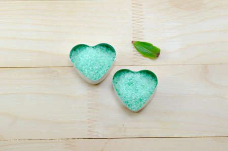 Green sea salt in a heart shaped box on a wooden table with a green leafの写真素材