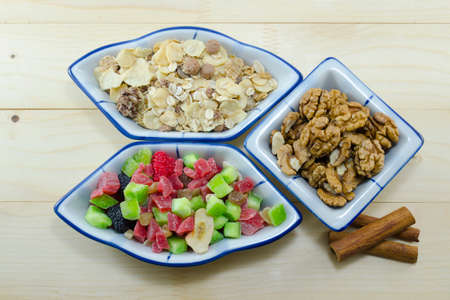Muesli, walnuts and dried fruit and cinnamon sticks on a wooden tableの写真素材
