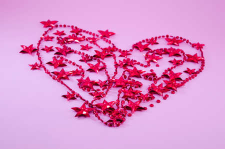 Heart made out of red Christmas tree pearls and stars on pink backgroundの写真素材