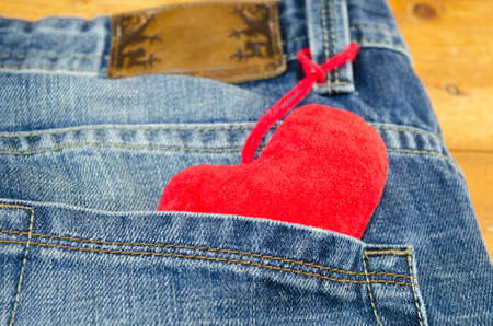 Red heart sticking out of a jeans back pocket lying on a wooden table