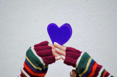 Girl in colorful mittens holding a purple heart against a white wallの写真素材