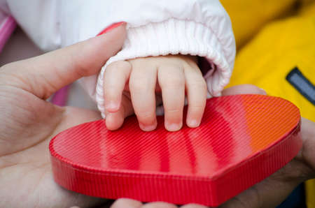 Baby's and mother's hand on a heart shaped boxの写真素材