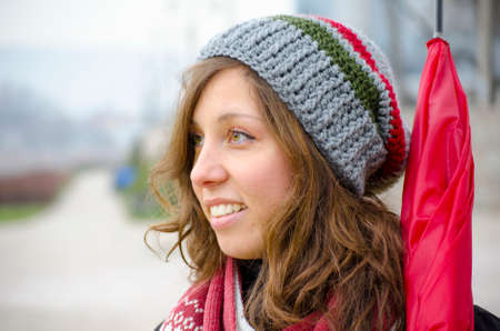 Young brunette wearing a hand made woolen hat and a red umbrella outdoors