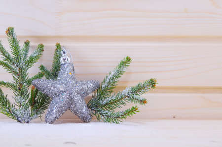 A shiny star ornament with fir branches on a wooden suface covered with snowの写真素材