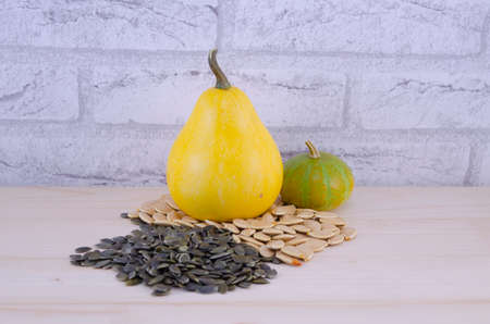 Colorful decorative pumpkins and pumpkin seeds on a wooden table with a brick wall in the background