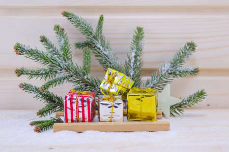Christmas presents on a sledge, with a fir branch in the background, on a wooden surface covered with snowの写真素材