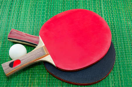 Two table tennis rackets and a ping pong ball on green surface