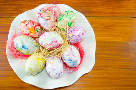 Bunch of hand colored Easter eggs on a white plate decorated with colorful straw