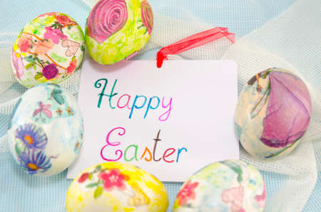 Bunch of handcolored decoupage Easter eggs around a handwritten greeting card saying "Happy Easter"の写真素材