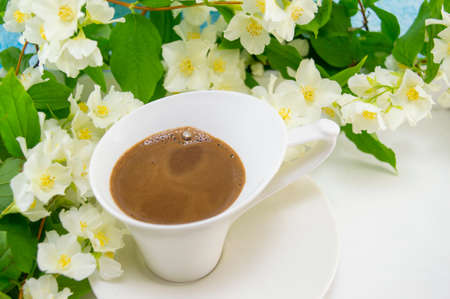 White cup of coffee on a wooden table decorated with flowers