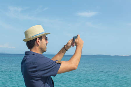 Man taking photos with his cell phone at the seaの写真素材