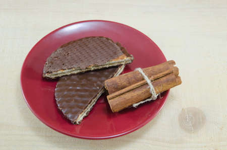 Chocolate biscuits on a red plate with cinnamon sticksの写真素材