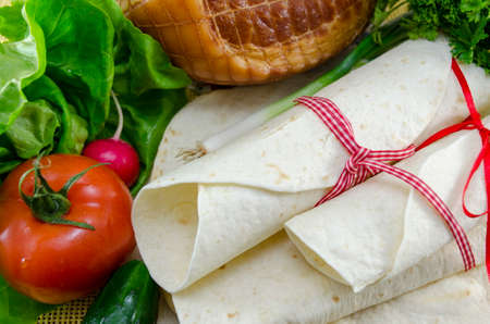Empty tortillas tied with a red ribbon on a table with tomato, lettuce and hamの写真素材