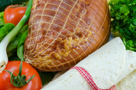 Empty tortillas tied with a red ribbon on a table with tomato, lettuce and hamの写真素材