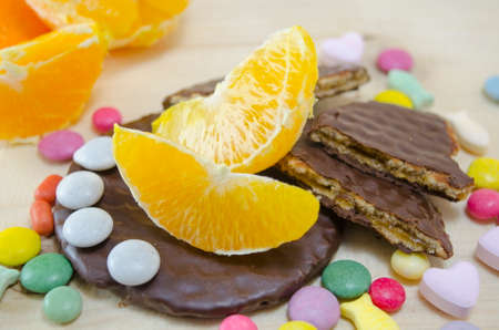 Fresh orange, biscuits and colorful bonbons on a wooden tableの写真素材