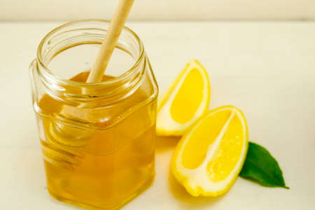 Jar of honey a wooden spoon and lemons on a tableの写真素材