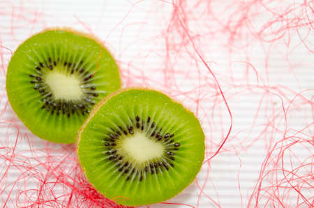 Halved kiwis on a white cardboard decorated with pink strawの写真素材