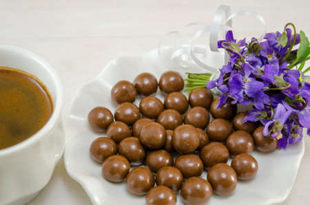 White cup of coffee with dessert on a wooden table decorated with flowersの写真素材
